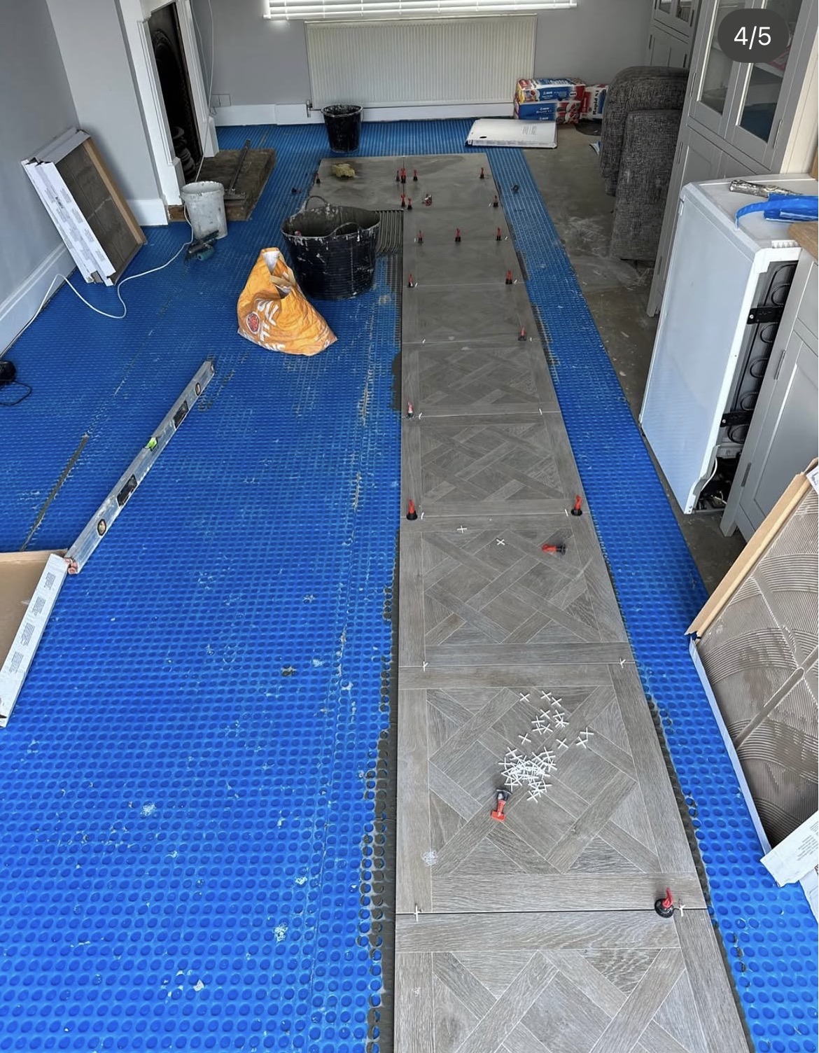 Patterned floor tiles being installed over a blue decoupling membrane